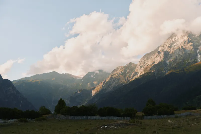 Tranquil mountain landscape with rugged peaks, blue sky and fluffy clouds. A vast valley below conveys outdoor exploration, nature appreciation, and serene travel vibes.