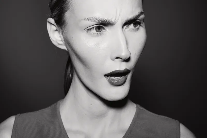 White woman with pale skin shows confused expression in black and white close-up portrait with dark background. Concept for emotion and doubt.