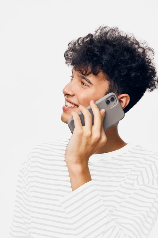 smiling man talking on smartphone with curly hair wearing striped shirt, looking sideways on white background in casual style, youth and communication concept