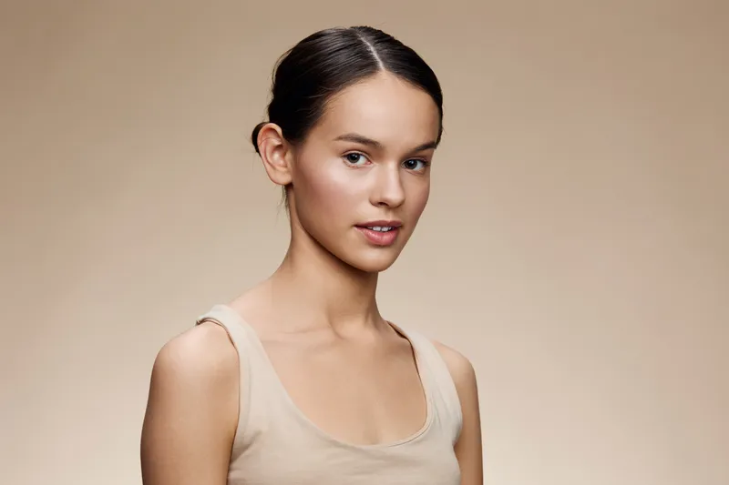 Young female model with a serene expression and a natural makeup look, against a soft beige background, perfect for beauty and wellness concepts