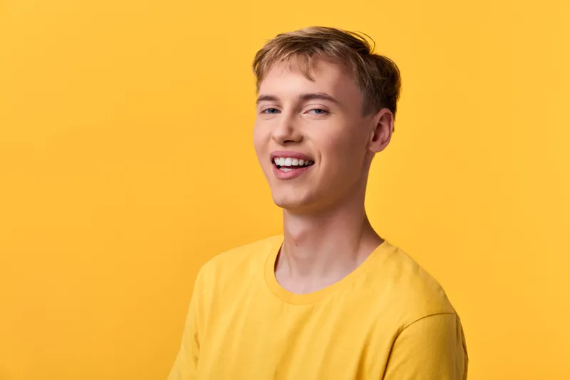 Smiling man in a yellow shirt stands against a vibrant yellow backdrop, radiating casual style, bright mood, and approachable energy for lifestyle, fashion, or marketing visuals.