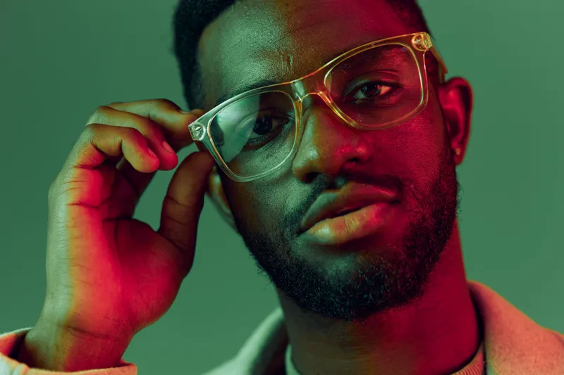 Portrait of a stylish Black man wearing glasses with expressive emotions and colorful lighting, perfect for fashion and lifestyle concepts