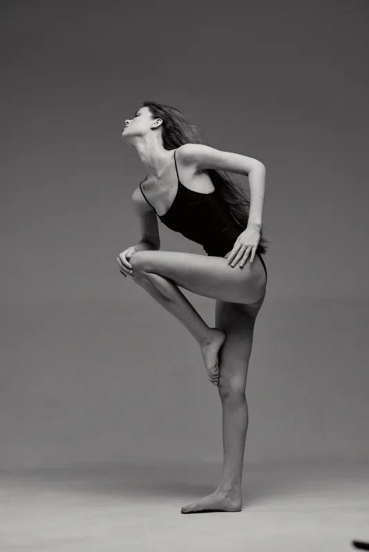 Black and white image of a graceful woman dancer in a poised pose wearing minimal attire.