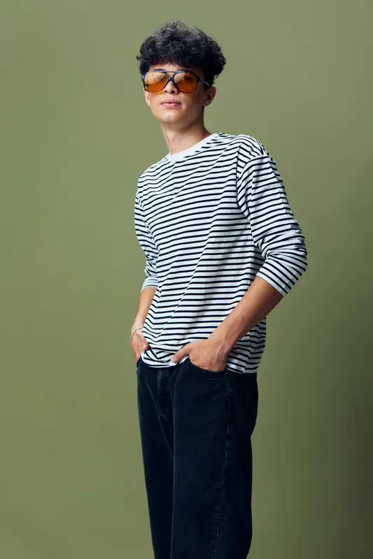 young man wearing sunglasses and striped shirt posing confidently with hands in pockets against olive green background, casual style portrait with relaxed mood