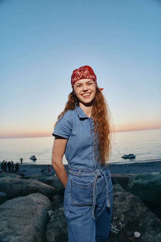 lifestyle woman in modern boho-western denim street style smiling outdoors by the sea at sunset with film color tones and casual outfit