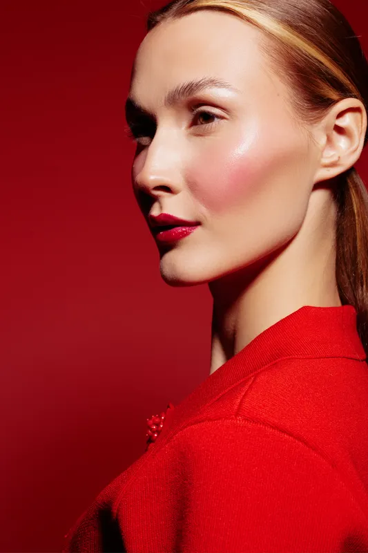 Close-up portrait of a young woman with glowing skin and red lipstick wearing a red outfit against a red background. Concept of beauty, fashion, makeup, and elegance.