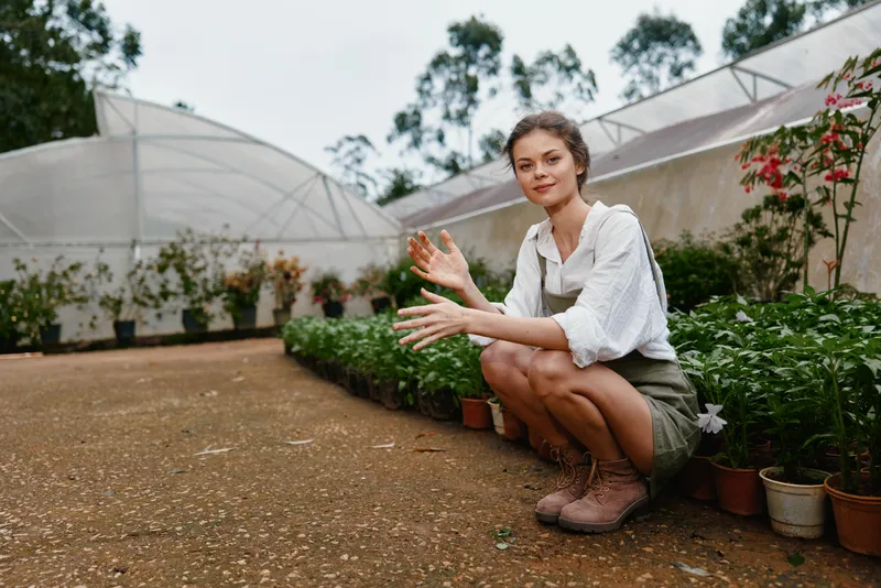 Young woman in a garden showcasing her passion for sustainable gardening with vibrant plants, wearing casual attire, smiling in a sunny environment