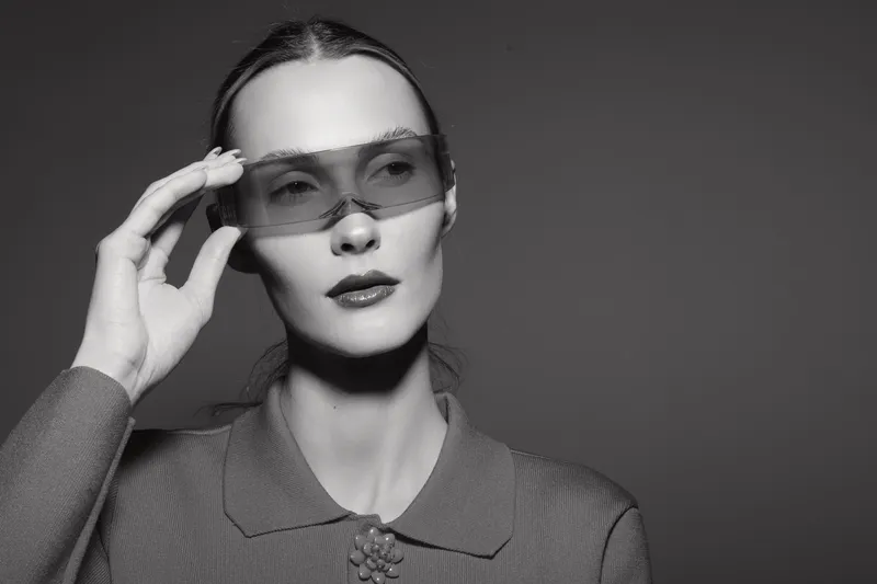 Portrait of a fair skinned Caucasian woman with slicked back hair wearing futuristic sunglasses and a textured blouse. Concept of fashion, style, and modern elegance.