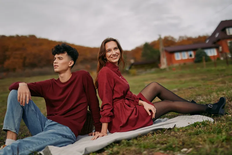 Young couple in matching autumn outfits relax outdoors on a blanket, sharing a candid, authentic moment of connection and ease, emphasizing authenticity and accuracy in the depiction of rural leisure.