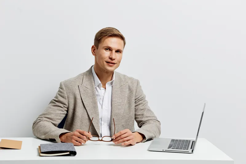 smiling young caucasian man sitting at desk wearing jacket using laptop for digital nomad work remote business concept casual style