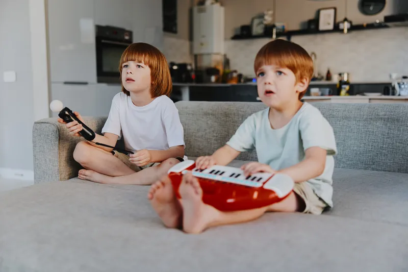 Two boys enjoying playtime together, engaged with musical instruments, displaying curiosity and excitement in a cozy living room setting. ###
