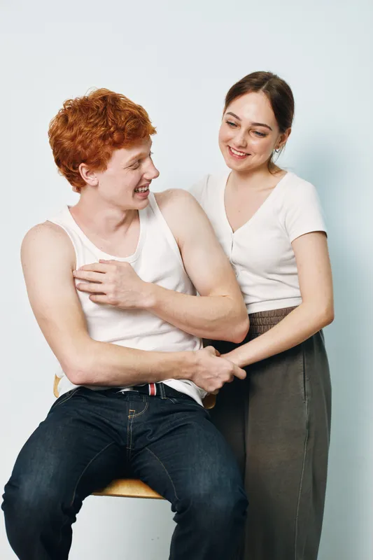 Young man and woman smiling and interacting, casual clothing, friendly moment, studio background, happiness and positive communication between two people.
