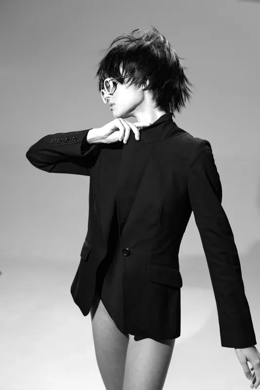 Black and white portrait of a stylish man wearing glasses and a blazer with artistic pose and edgy hairstyle.