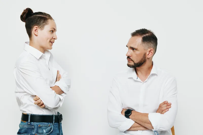 A professional man and colleague stand with arms crossed, showing confident and thoughtful emotions against an isolated color background.