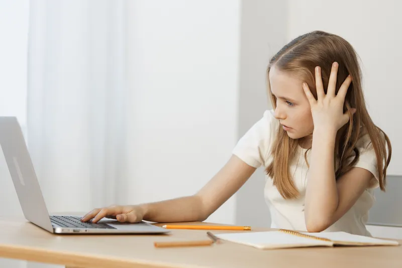 A young girl looking frustrated at her laptop, reflecting the challenges of online learning and concentration issues in a minimalistic, bright setting