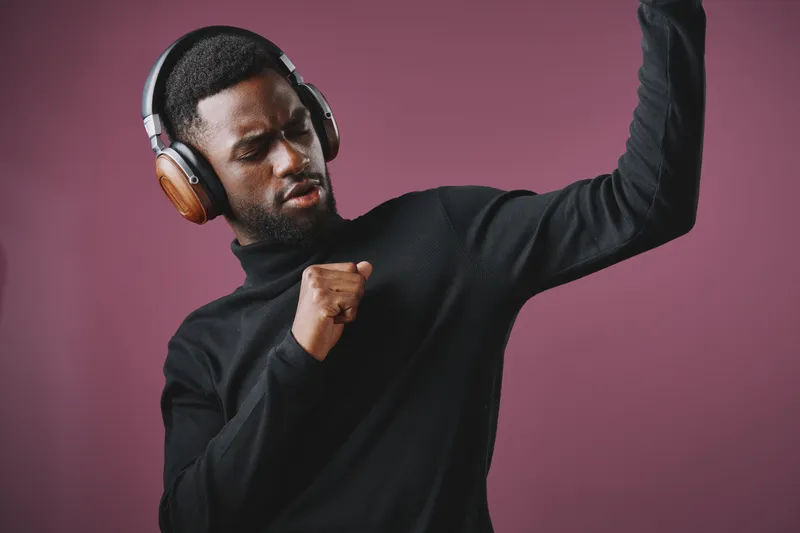 Young Black man enjoying music with headphones and dancing joyfully against a purple background, showcasing vibrant emotions and style