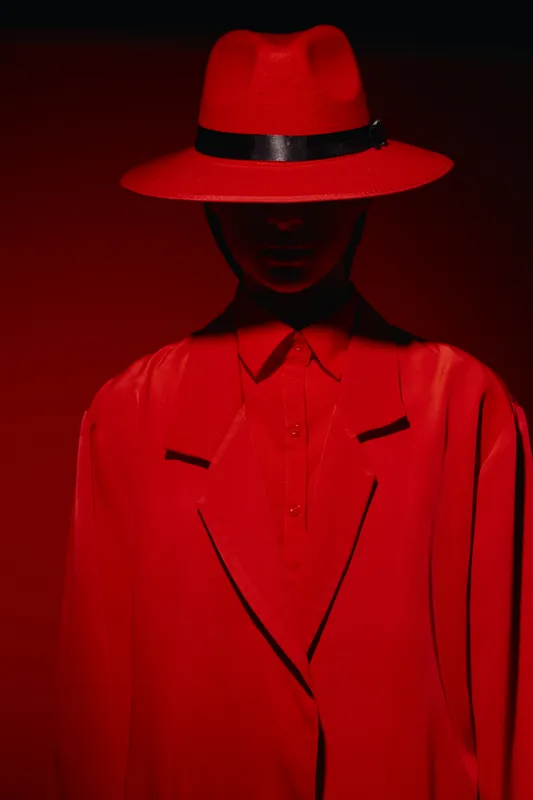 Mysterious figure in a bright red hat and coat poses against a red backdrop. The dramatic contrast and shadow merge to create a bold fashion statement. Creative beauty concept.
