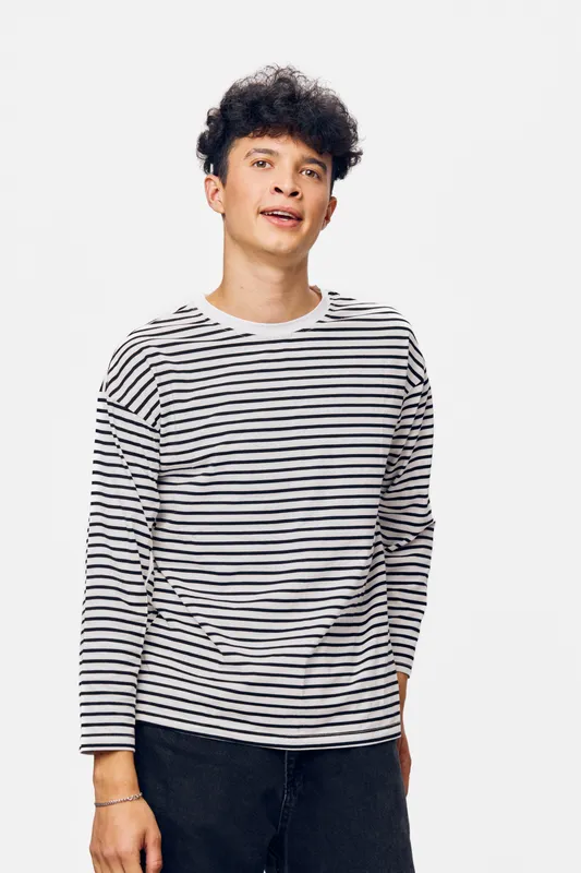 young man wearing a striped long sleeve shirt standing against white background with casual pose and natural expression in a minimalistic studio setting