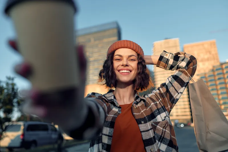Woman smile coffee shopping urban candid beanie portrait: a joyful moment of authenticity and mindful living, golden hour glow and emotional storytelling in a casual city street scene.