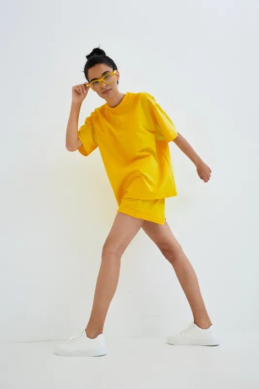 young woman in yellow outfit and glasses walking confidently against white background, casual style and modern fashion look