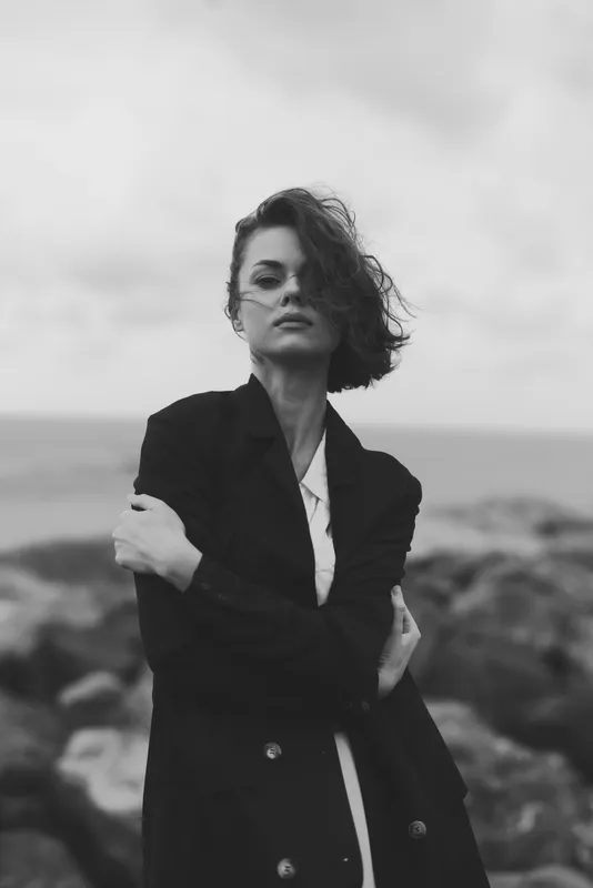 Moody monochrome scene with a woman in a coat on a windy sea shore, windswept hair and a strong silhouette, conveying outdoor fashion and artistic mood for editorial use and campaigns