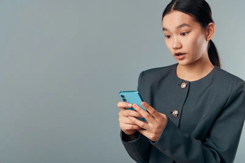 Young woman, portrait and surprised expression with smartphone in hands on grey background. Casual business style, communication and technology for message reaction or social media.