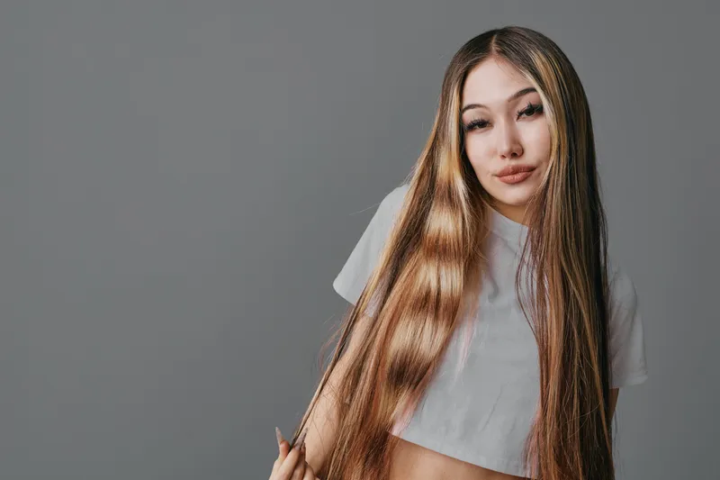 Young woman with long straight hair wearing white t shirt posing with gray background. Attractive female model with natural makeup and casual style looking at camera confidently.