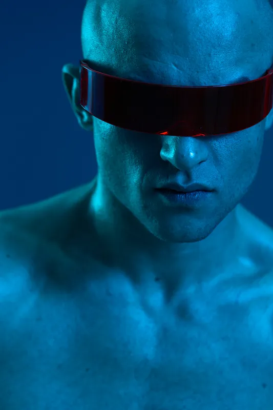 Futuristic man with visor in a striking blue light, showcasing strong emotions and an intense look. Perfect for themes of technology, innovation, and modernity.