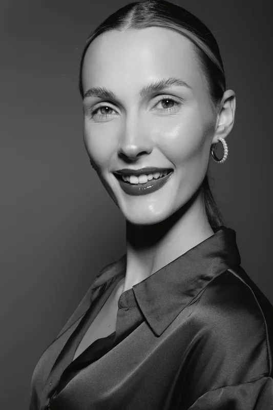 Smiling caucasian woman with fair skin in shiny blouse poses in black and white studio portrait. Concept of elegance, beauty, and confidence.