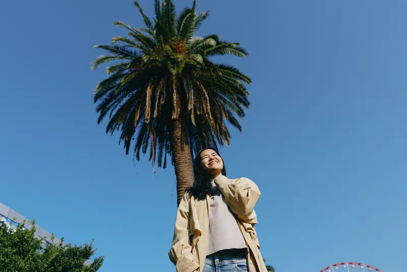 Palm, tree, woman, outdoor, sky, casual, fashion, urban, summer, landscape, candid pose beneath a clear blue horizon with modern greenery, highlighting streetwear style and a relaxed, confident mood