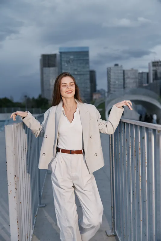 Confident woman in business attire smiling against a city backdrop, expressing positivity and professionalism in a modern urban setting.