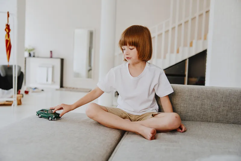 Young boy playing with a toy car in a bright living room, showcasing creativity and joy in a modern home setting with minimalistic decor.