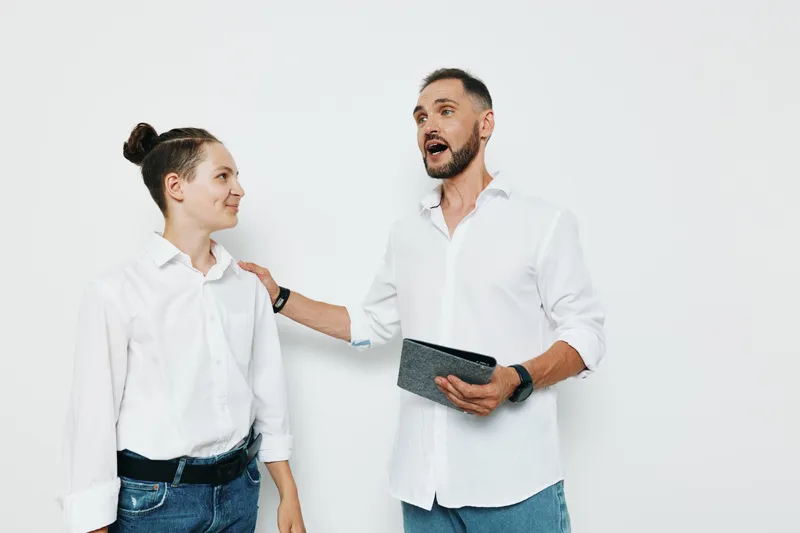 A confident male business professional speaks with enthusiasm to a colleague against a plain isolated colored background, gesturing with a tablet while showing energy, focus, and engagement.