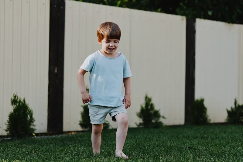 Happy boy playing outdoors in bright summer day, wearing light clothes, exploring the garden with excitement and joy, expressing pure innocence and fun.
