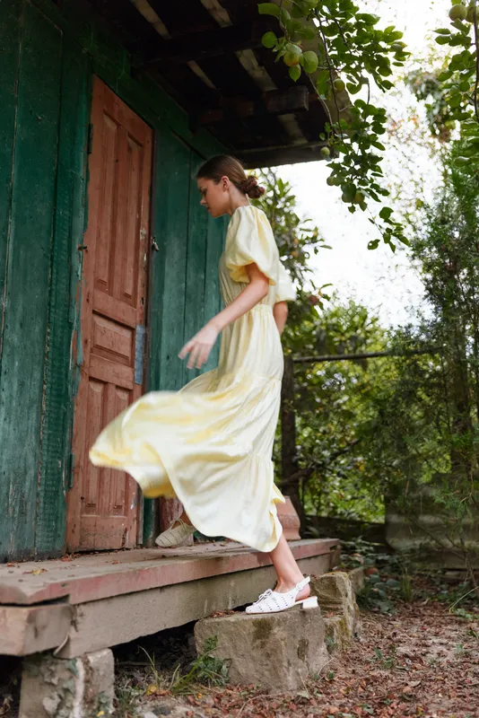Woman in yellow dress stepping up wooden porch of rustic house, candid rural scene showing authenticity and inclusivity in vintage life