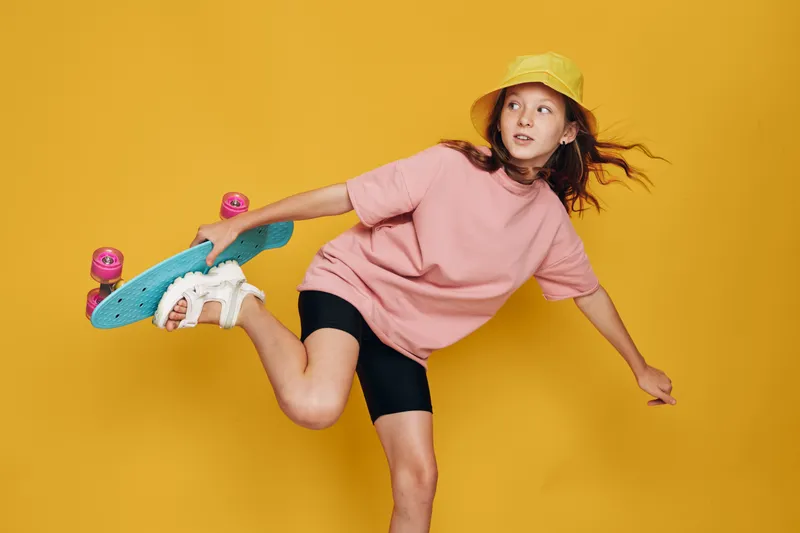 Young girl in a yellow hat performs a dynamic skateboarding trick against a bright yellow background. Motion and youth concept.