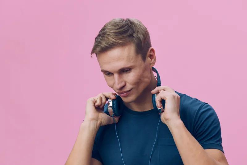 Close-up of a young smiling man with short hair wearing blue t-shirt and headphones isolated on pink background, casual, cheerful expression, leisure, trendy style, lifestyle concept.