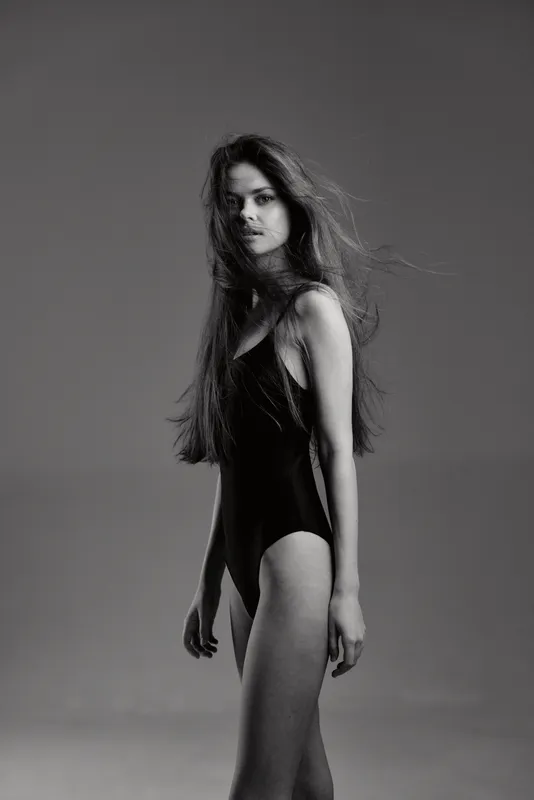 Black and white portrait of a young woman with long hair in a black bodysuit looking confidently