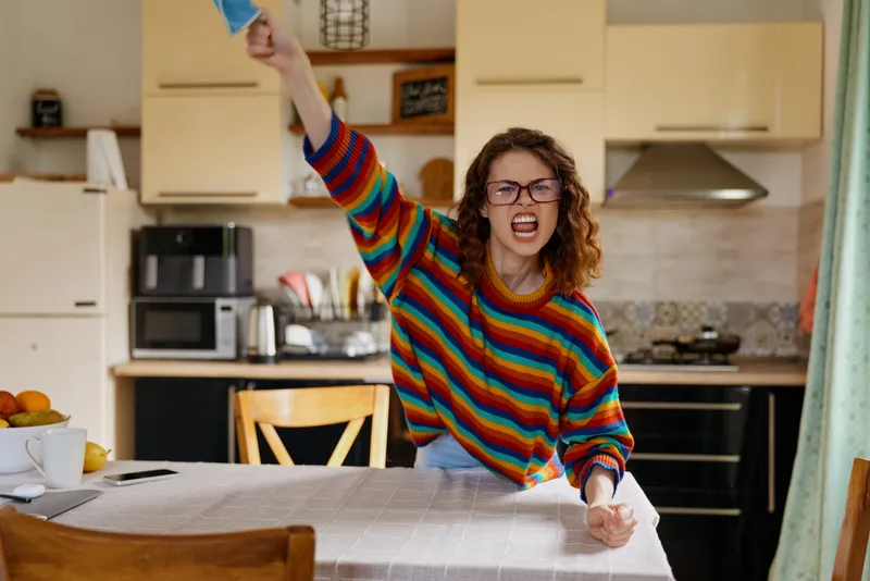 Vivid woman indoors, expressive moment at a kitchen table, striped sweater, casual home lifestyle, warm natural light, cluttered counter, dynamic emotion captured