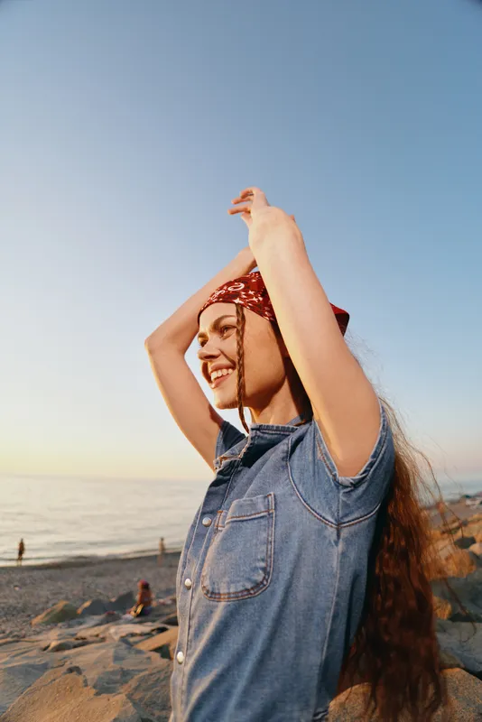 lifestyle woman in modern boho-western denim street style smiling outdoor with film color tone on sunny beach background during golden hour