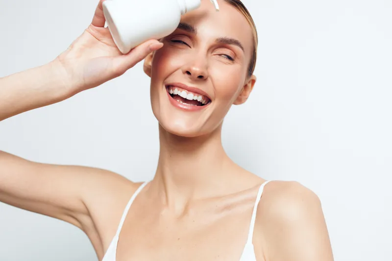 Woman skincare beauty face cream smile applying treatment hygiene wellness, happy caucasian woman applies face cream with bottle, smiling on light background, gentle home skincare routine
