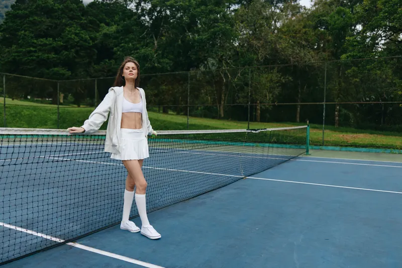 Stylish young female tennis player in a sporty outfit with a confident expression, standing near the net on a sunny day, perfect for sports and fitness concepts