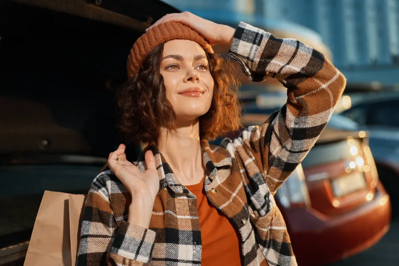 Woman portrait shopping by a car trunk in urban streetwear, beanie and plaid jacket at golden hour. Candid lifestyle moment with authenticity, golden hour glow and emotional storytelling.