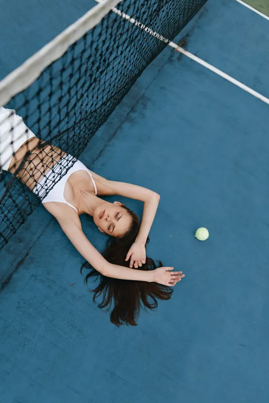 Young female athlete resting on a tennis court, showcasing a relaxed pose, sporty attire, and vibrant colors, symbolizing vitality and energy in sports