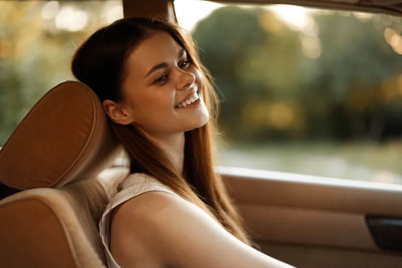 A young woman enjoying the warm sunlight in her car, exuding happiness and serenity with her long hair cascading over her shoulder.