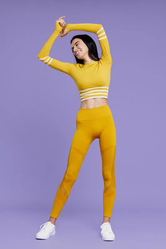 Fit woman sport fitness stretching in bright yellow activewear with happy expression, isolated on purple background, promoting health and energy.