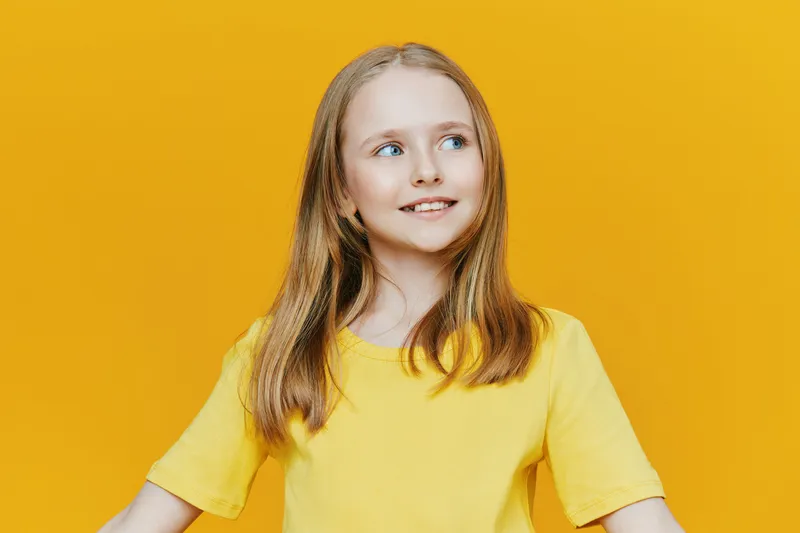 Young girl with long hair smiling against a vibrant yellow background, wearing a bright yellow t shirt, conveying happiness and positivity in a cheerful atmosphere