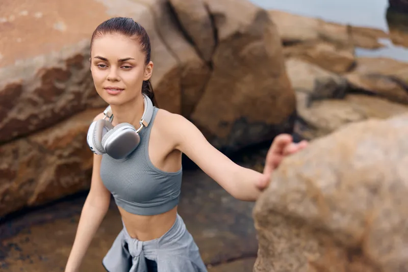 Young woman exercising outdoors in sportswear with headphones, showcasing a healthy lifestyle and natural beauty against a rocky background