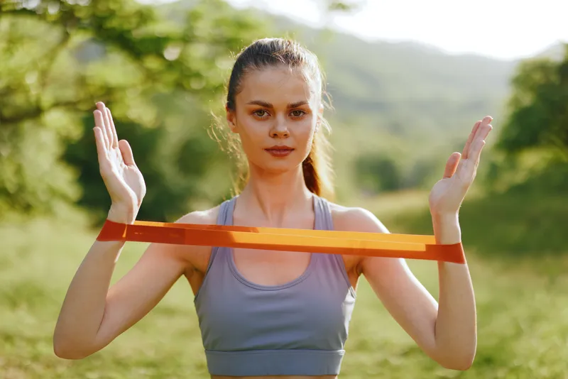 Young athletic woman exercising outdoors with a resistance band, showcasing strength and determination in a natural setting