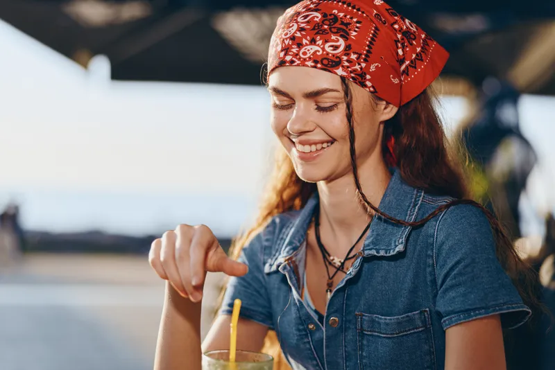lifestyle woman in modern boho-western denim street style smiling outdoors with red bandana and natural sunlight in film color aesthetic, casual summer mood
